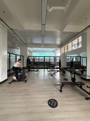 Academia com equipamentos de ginástica, uma pessoa usando uma máquina elíptica e um banco de pesos.