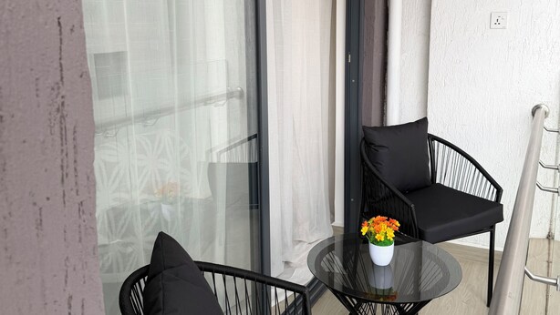 A balcony with two black chairs, a small round table with a vase of flowers, and a glass door leading to a room. - Cozy & Stylish Apartment with stunning views, 2 minutes from yaya center. (Nairobi)
