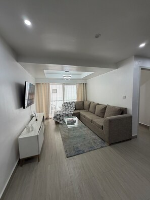 Uma sala de estar moderna com sofá, mesa de centro, televisão na parede e uma poltrona estampada.