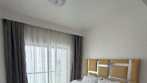 A bedroom with a large bed, a nightstand, and a window with curtains. - Cozy & Stylish Apartment with stunning views, 2 minutes from yaya center. (Nairobi)