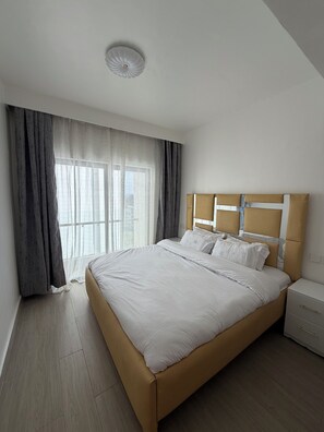 Quarto com uma cama grande, uma mesinha de cabeceira e uma janela com cortinas.