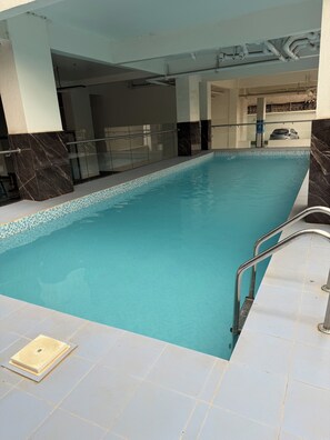 An indoor swimming pool with clear water, a tiled floor, and a metal ladder. - Cozy & Stylish Apartment with stunning views, 2 minutes from yaya center. (Nairobi)