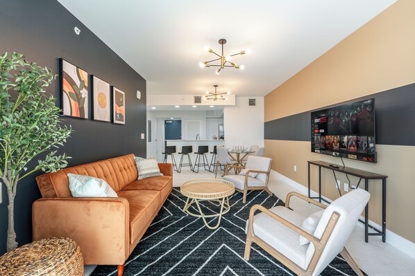 Ein modernes Wohnzimmer mit einer Couch, Sesseln, einem Couchtisch und einem an der Wand befestigten Fernseher.