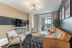 Ein modernes Wohnzimmer mit einer Couch, Sesseln, einem Couchtisch und einem flachbildfernseher an der Wand.