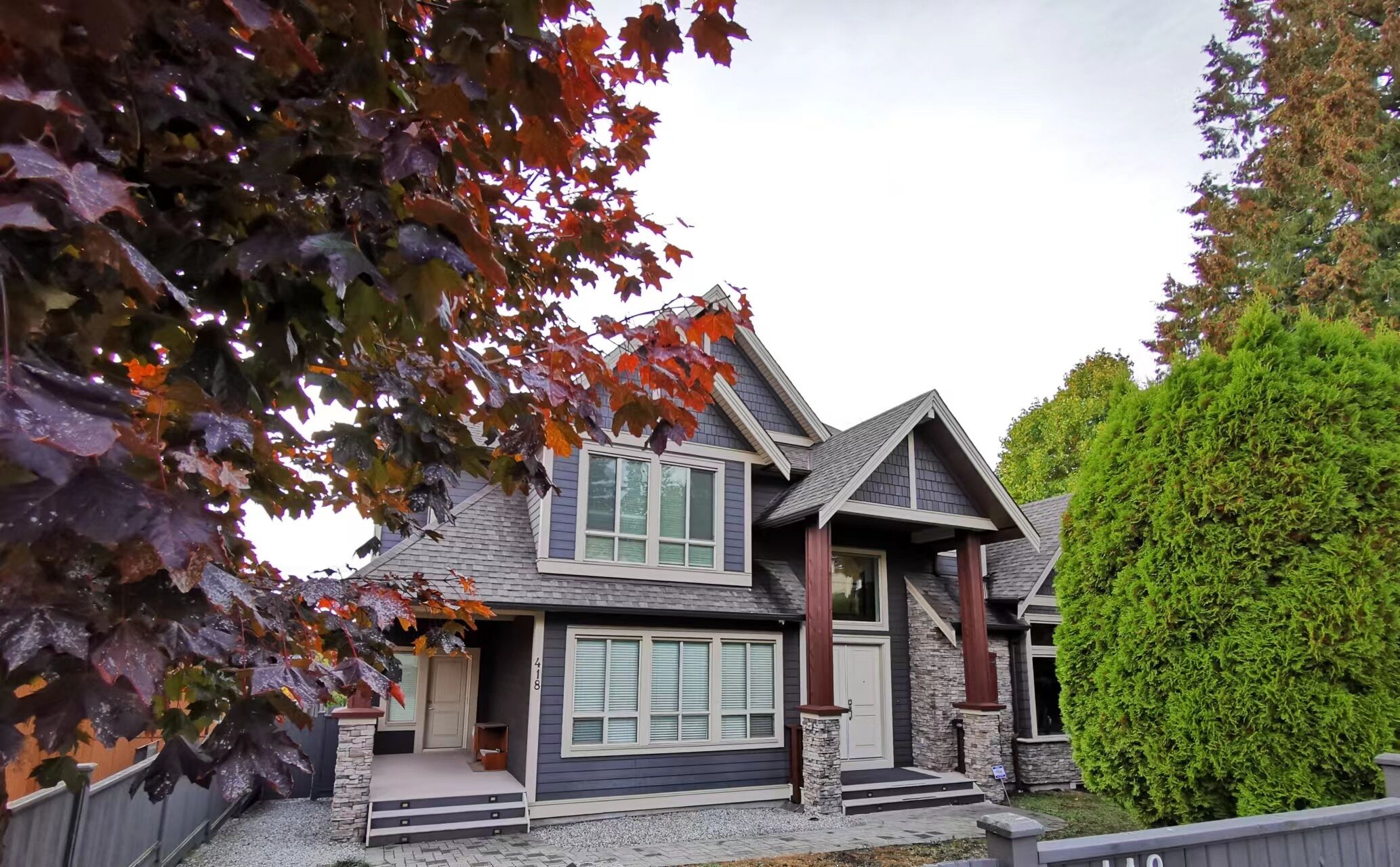 A two-story house with a stone foundation, a grey roof, and a garage with a white door.