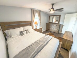 A bedroom with a bed, a dresser, a mirror, a ceiling fan, and a door.