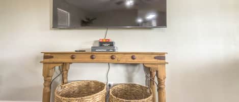 Ein Zimmer mit an der Wand befestigtem Fernseher, einem Holzkonsole-Tisch mit zwei Körben und einem Monopoly-Spiel auf der Oberseite.