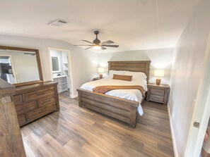 A bedroom with a wooden bed, nightstands, a dresser, a ceiling fan, and a large mirror.