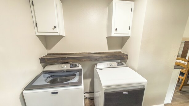 A laundry room with two front-loading washing machines and two cabinets above them. - Brittleville Bunkhouse: Peaceful Country Getaway (Brooksville)