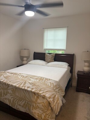 Un dormitorio con una cama, ventilador de techo, ventana con persianas y dos lámparas de noche.