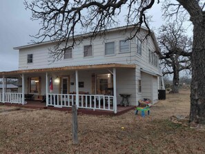 A two-story house with a porch, a flag, and a small table. - Rustic Getaway on 3.5 acres w/Hot tub Near Lake and state park (Buchanan Dam)