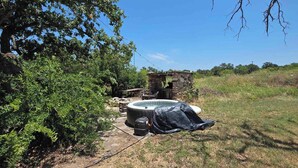 A hot tub outdoors with a stone structure nearby, surrounded by greenery.