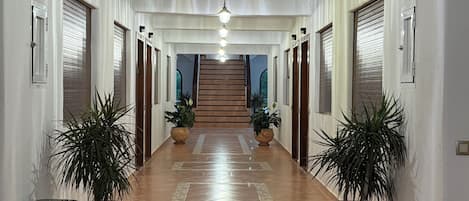 A hallway with a tiled floor, potted plants, and a staircase leading to an upper level.