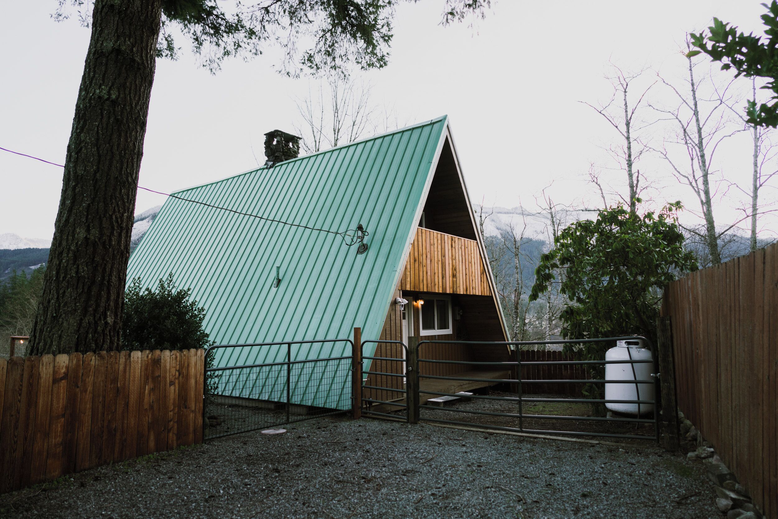 A triangular metal-roofed cabin with a wooden front door and a gravel driveway.