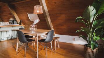 A wooden interior with a dining table, chairs, a hanging light fixture, and a potted plant.