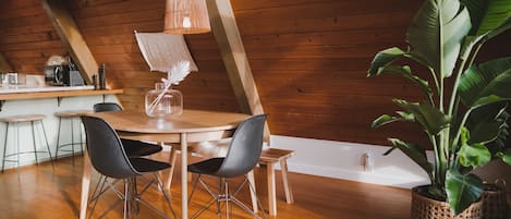 A wooden interior with a dining table, chairs, a hanging light fixture, and a potted plant.