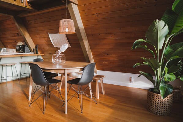 A wooden interior with a dining table, chairs, a hanging light fixture, and a potted plant.