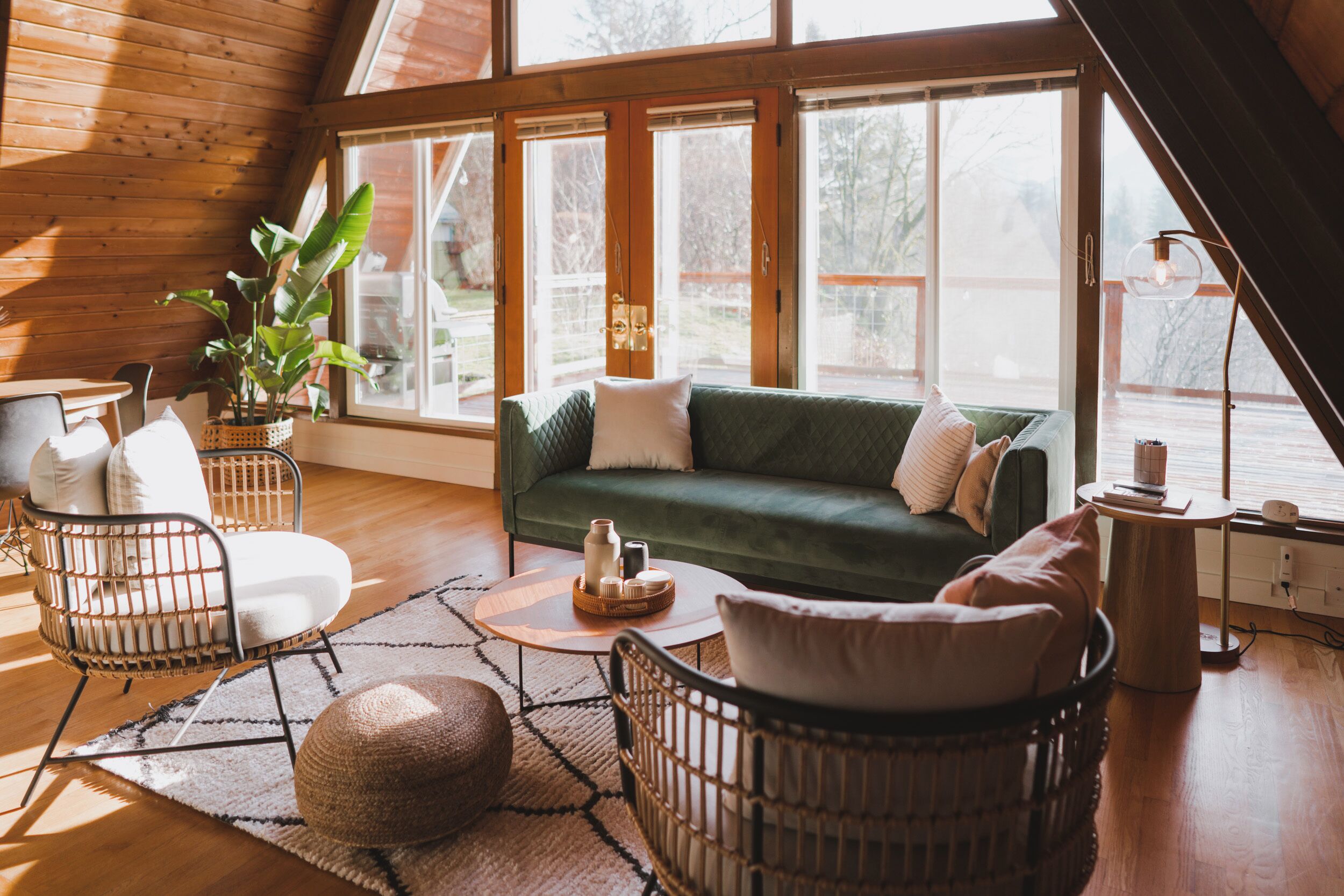 Une pièce confortable de style loft, avec un canapé vert, des fauteuils en osier et une grande fenêtre donnant sur l’extérieur.