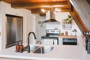 A modern kitchen with a stainless steel refrigerator, a black stove, and a dishwasher. - PNW A-Frame - Hot tub with view and A/C (Gold Bar)
