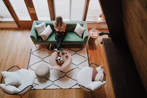 A room with a green sofa, two white armchairs, a round coffee table, and a patterned rug. - PNW A-Frame - Hot tub with view and A/C (Gold Bar)