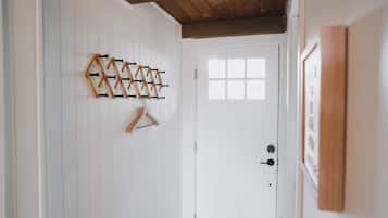 A hallway with a wooden ceiling, a white door with a window, and a wall-mounted coat rack.