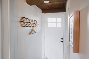 A hallway with a wooden ceiling, a white door with a window, and a wall-mounted coat rack.