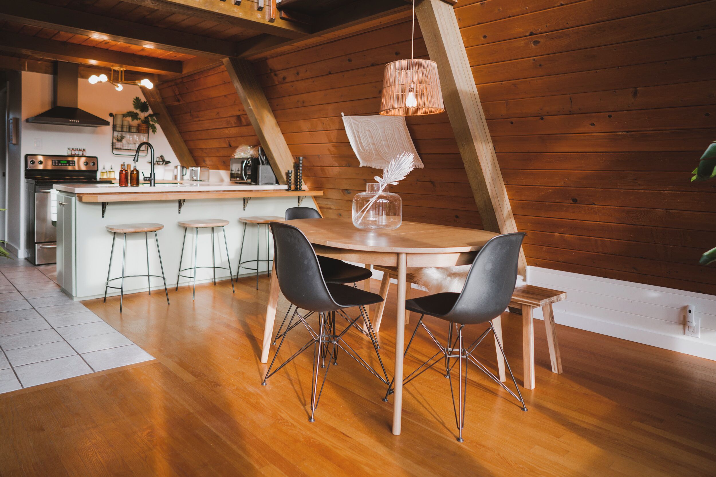 A modern kitchen with a wooden ceiling, a central island with stools, and a hanging light fixture.