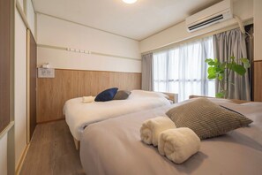 Ein Hotelzimmer mit zwei Betten, einem Holzkopfteil, einem Fenster mit Vorhängen, einer Klimaanlage und einer Pflanze.