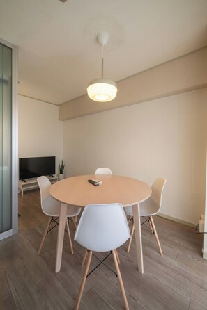 Ein moderner Essbereich mit einem runden Tisch, weißen Stühlen, einem Fernseher und einer Deckenleuchte.