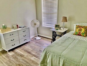 Ein Schlafzimmer mit einem Bett, einem Schminktisch, einem Schreibtisch, einer Lampe und einem Fenster mit Jalousien.
