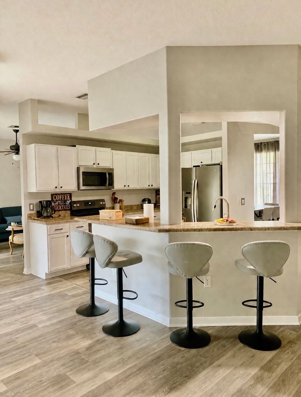 A modern kitchen with white cabinets, a central island with bar stools, a microwave, and a refrigerator.