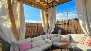 An outdoor seating area with a wooden pergola, cushioned sofas, and round wooden tables.