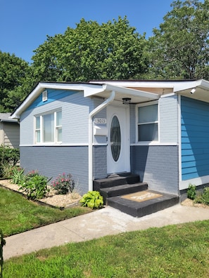 Una casa de un piso con fachada azul, una puerta principal con panel de vidrio y un cartel con el número 3013.