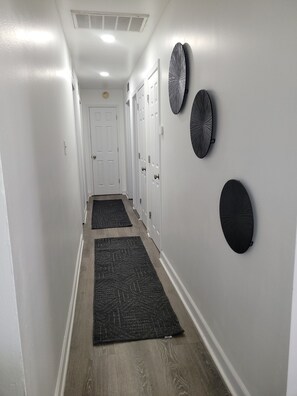 Un pasillo con piso de madera, paredes blancas y dos alfombras negras.