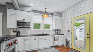A kitchen with white cabinets, a stainless steel stove, a microwave, and a hanging light fixture. - Luxury Modern 30+ Day Bungalow. Walk Downtown. Hot Tub. Pet Friendly (Yellow Springs)