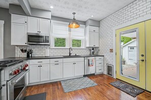 A kitchen with white cabinets, a stainless steel stove, a microwave, and a hanging light fixture. - Luxury Modern 30+ Day Bungalow. Walk Downtown. Hot Tub. Pet Friendly (Yellow Springs)