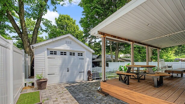 A covered patio area with a wooden deck, a white garage, and a small garden with potted plants. - Luxury Modern 30+ Day Bungalow. Walk Downtown. Hot Tub. Pet Friendly (Yellow Springs)