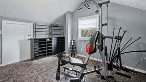 A home gym with a ceiling fan, a pull-up bar, a bench press, and a window with blinds. - Luxury Modern 30+ Day Bungalow. Walk Downtown. Hot Tub. Pet Friendly (Yellow Springs)