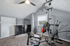 A home gym with a ceiling fan, a pull-up bar, a bench press, and a window with blinds. - Luxury Modern 30+ Day Bungalow. Walk Downtown. Hot Tub. Pet Friendly (Yellow Springs)