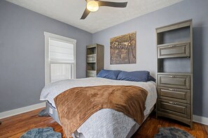 Ein Schlafzimmer mit einem Bett, einem Deckenventilator, einer Kommode und einem Gemälde an der Wand.