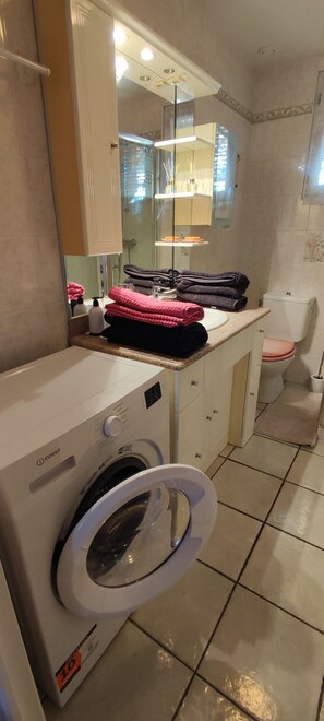 Ein kleines Badezimmer mit Waschmaschine, Toilette und Spiegel.