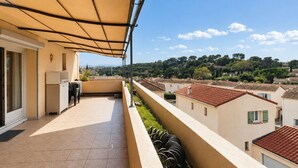 A balcony with a retractable awning, a sliding glass door, and a small table with chairs. - T2 climatisé avec vue proche de Cannes et Grasse (Mouans-Sartoux)