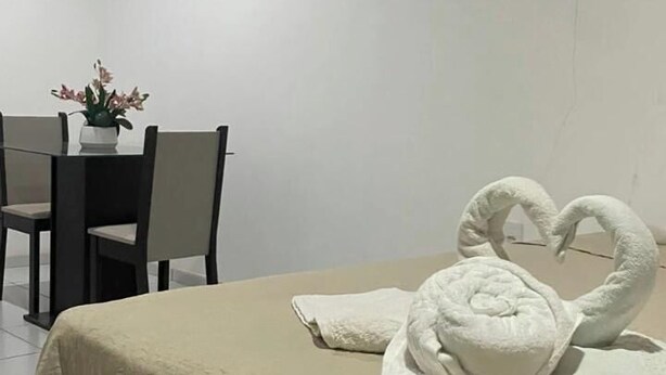 A hotel room with a bed, a table with chairs, and a vase with flowers. - Morada do vento  (São Miguel do Gostoso)