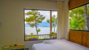 A bedroom with a large window offering a view of trees and a body of water.