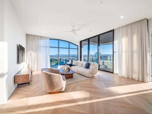 A spacious living room with a large window, a sofa set, a coffee table, and a flat-screen TV mounted on the wall. - The Arches by Aryve | Surfers Paradise (Surfers Paradise)