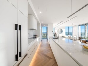 A modern kitchen with a central island, white cabinetry, and a view to the outdoors. - The Arches by Aryve | Surfers Paradise (Surfers Paradise)
