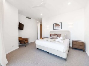 A modern bedroom with a bed, a chair, a bedside table, and a wall-mounted TV. - The Arches by Aryve | Surfers Paradise (Surfers Paradise)