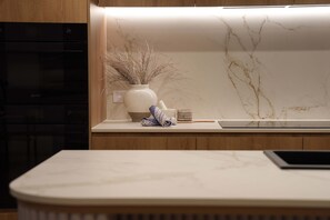 Eine Küche mit weißer Marmor-Spritzschutzleiste, einer weißen Vase mit Trockenpflanzen, einem eingerollten Stofftuch und einem Holzschneidebrett.