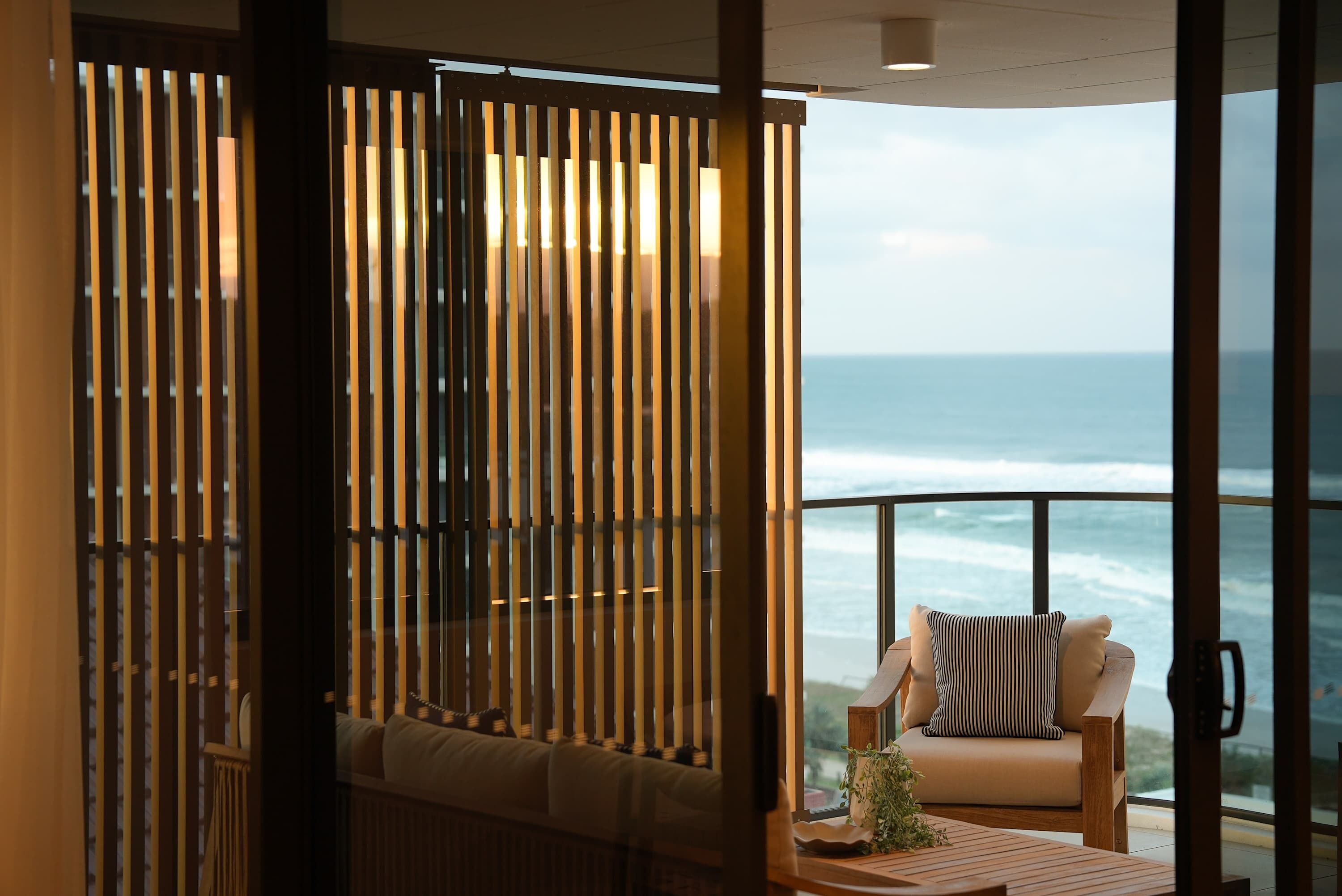 A room with a view of the ocean, a sofa with striped cushions, and a wooden table with a plant.