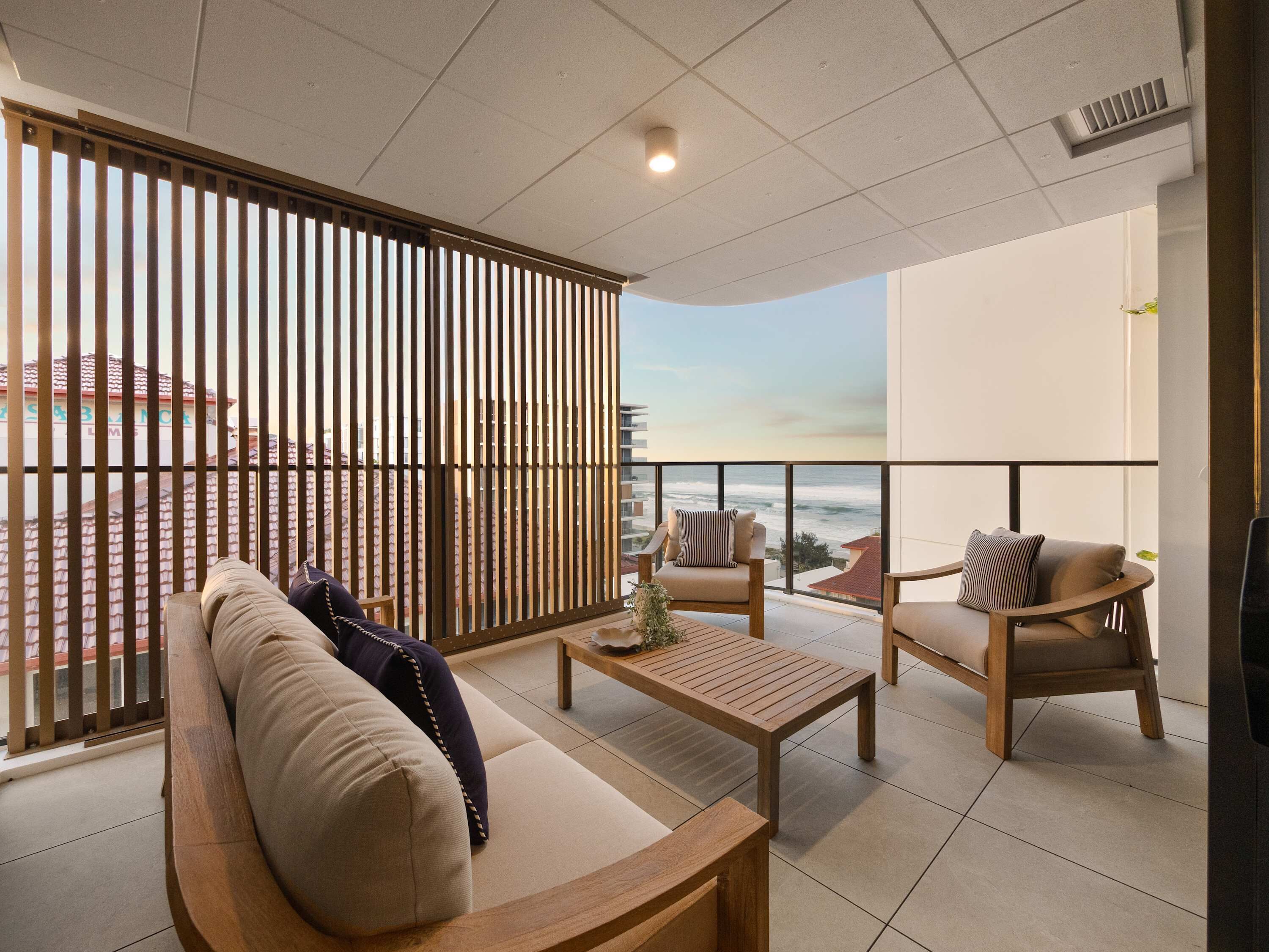 Un balcón moderno con sofá, sillas y una mesa, con vistas a la costa.